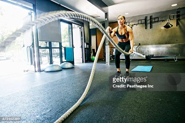 mixed race woman working out with heavy ropes in gymnasium - ausdauer stock-fotos und bilder