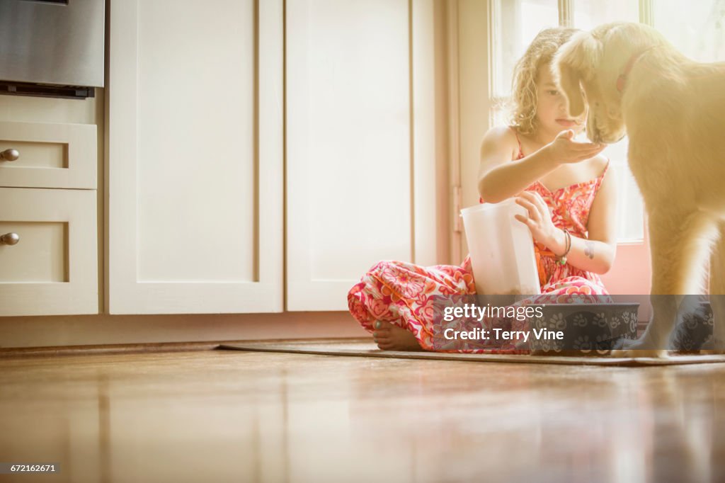 Caucasian girl sitting on kitchen floor feeding dog