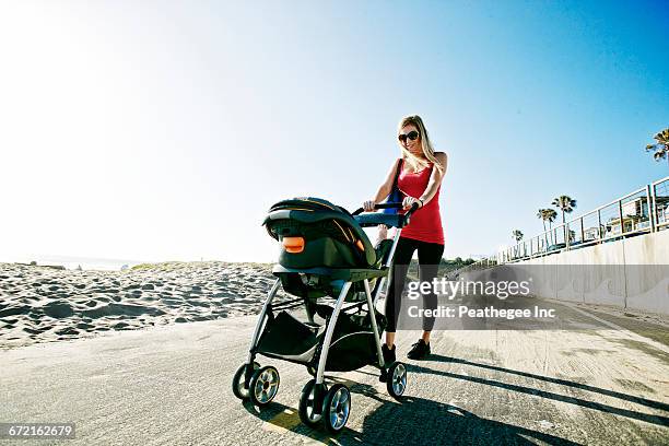 mother pushing baby son in stroller at beach - mother stroller stock pictures, royalty-free photos & images