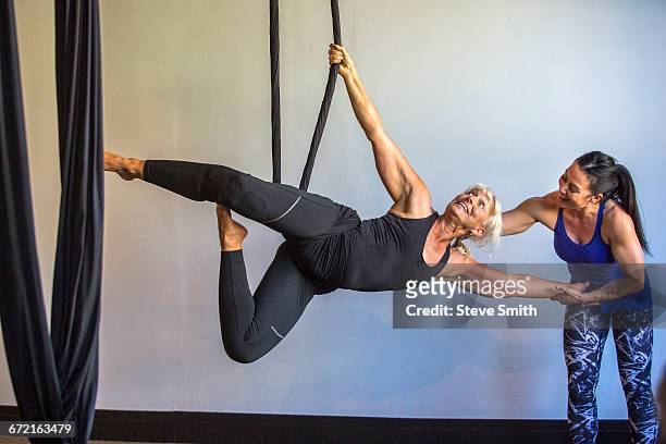 Instructor assisting yoga student hanging from silks