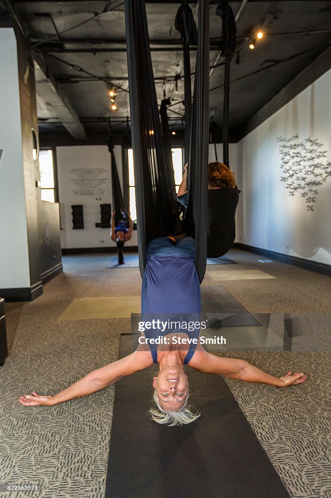 Caucasian woman performing yoga hanging from silks