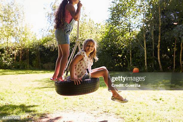 two girls on a tyre swing, one looking to camera, close up - tyre swing stock pictures, royalty-free photos & images