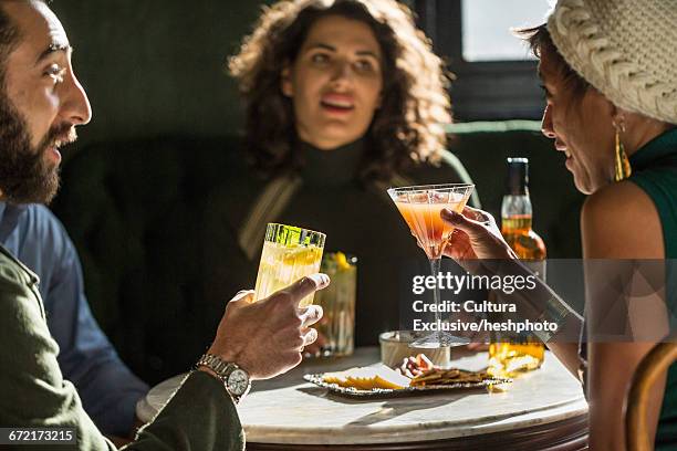 adult friends drinking cocktails at table whilst socialising in recreational bar - heshphoto - fotografias e filmes do acervo