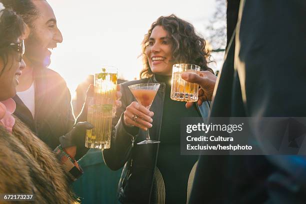 four adult friends socialising and drinking cocktails at recreational bar patio - cocktails stock pictures, royalty-free photos & images