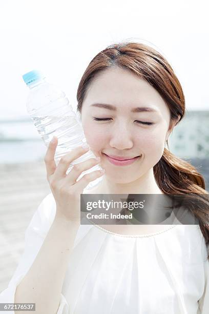 young woman touching water bottle on her cheek - hand holding a bottle stock pictures, royalty-free photos & images