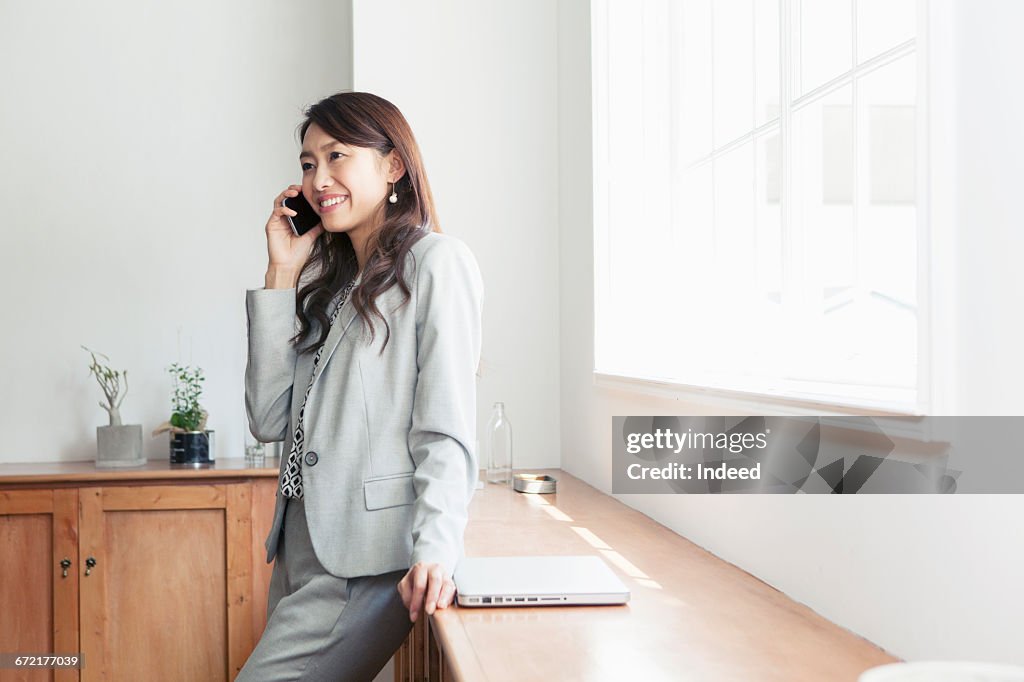 Young businesswoman talking on mobile phone by window