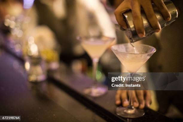 一個巴拿馬酒保的手, 把髒馬提尼倒入玻璃杯。 - dirty martini 個照片及圖片檔