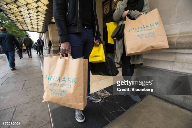 Shoppers hold carrier bags from Primark clothing store, operated by Associated British Foods Plc, outside the Selfridges Ltd. Department store on...