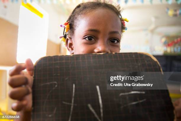 Dano, Burkina Faso An African child poses in a classroom at a school of the Dreyer Foundation and holds a chalkboard in his hands. Here children are...