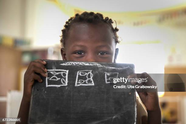 Dano, Burkina Faso An African child poses in a classroom at a school of the Dreyer Foundation and holds a chalkboard in his hands. Here children are...