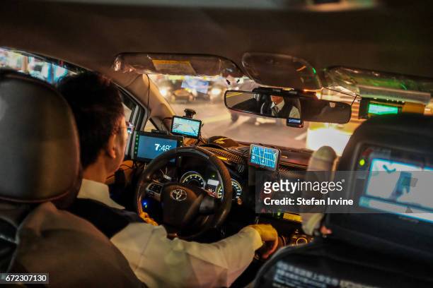 Taxi driver in night-time Taipei, with an array of technology devices installed on his car's dashboard.