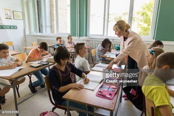 smiling teacher helping little boy with assignment in the classroom. - workbook stock pictures, royalty-free photos & images