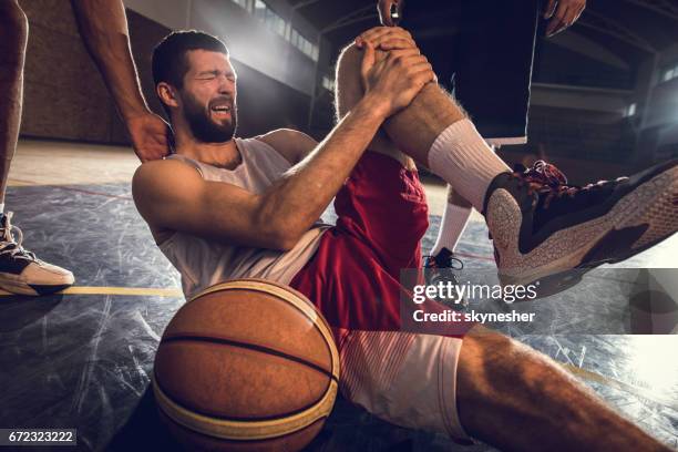 injured basketball player holding his leg in pain on the court. - injured knee stock pictures, royalty-free photos & images