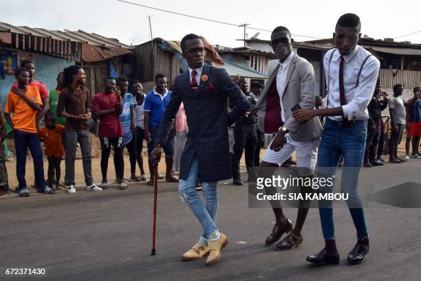 Members of La SAPE movement parade in a street of Abidjan on April 24, 2017 during a day of tribute to late Congolese rumba star Papa Wemba as part...