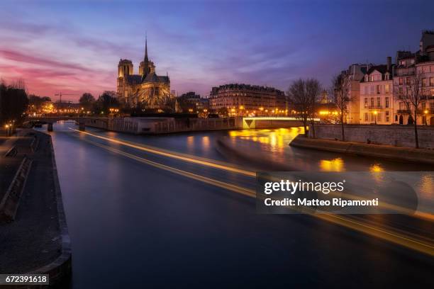 cathedral of notre dame de paris with seine river at sunset and light trails of boats - capitali internazionali fotografías e imágenes de stock