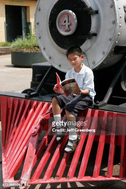 An Asian boy sat on the front of a train reading a book at the Huntsville Depot Museum.