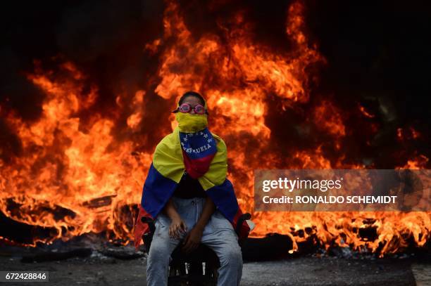 Venezuelan opposition activist is backdropped by a burning barricade during a demonstration against President Nicolas Maduro in Caracas, on April 24,...