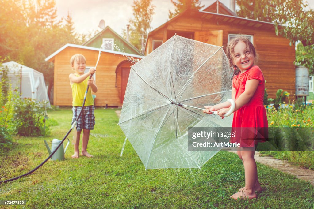 Happy girl and boy playing with sprinkler and umbrella