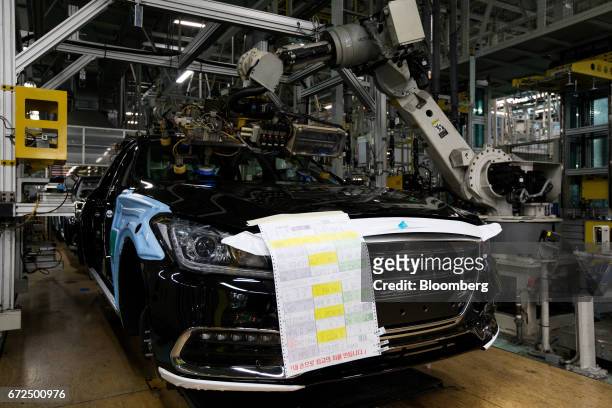 Robotic arm installs a windscreen glass panel onto a Hyundai Motor Co. Genesis luxury sedan on the production line at the company's plant in Ulsan,...
