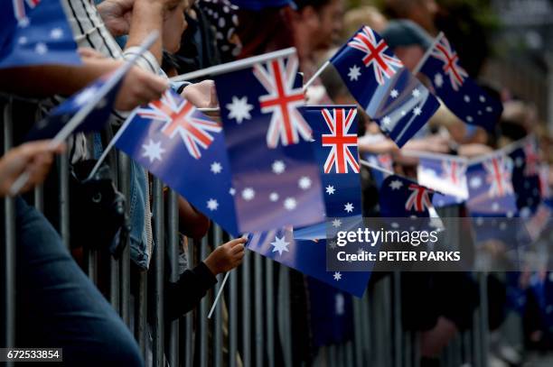 People wave Australian flags as they watch the Anzac Day parade in Sydney on April 25, 2017. - Ceremonies are held annually on the April 25...