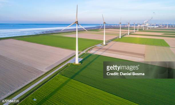 wind turbines lined up along coast towards industrial area - bouwwerk foto e immagini stock