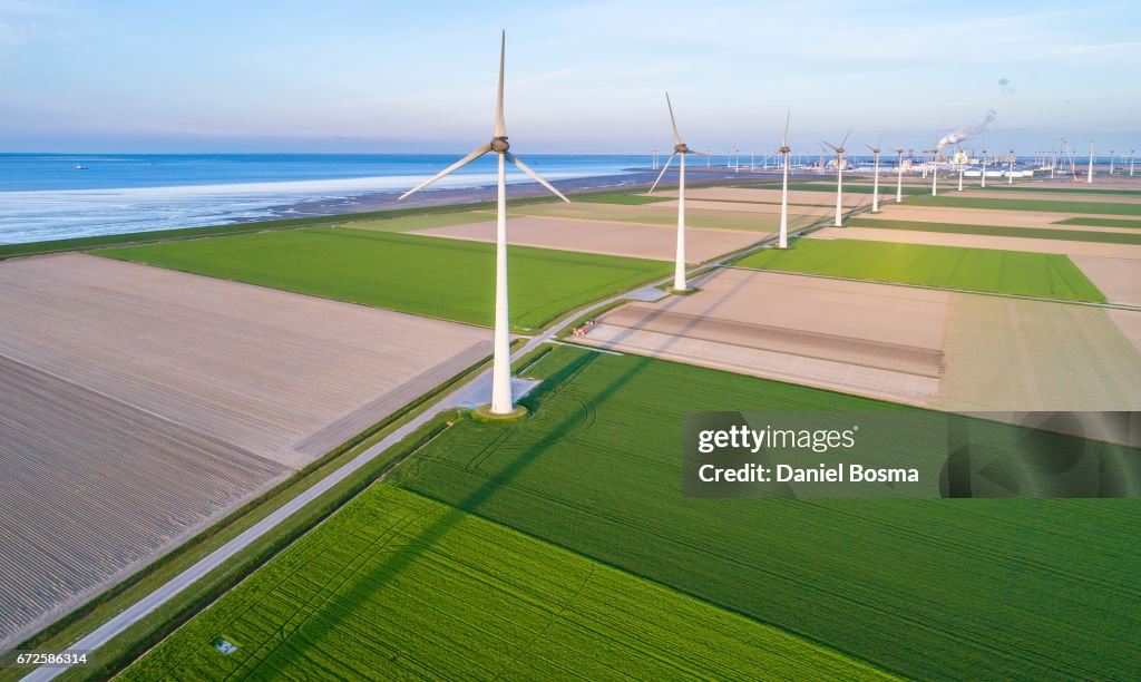 Wind turbines lined up along coast towards industrial area
