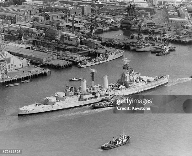 The Royal Navy Town-class light cruiser HMS Belfast under tow from tugboats passes the18th century 104-gun first-rate ship of the line and Admiral...