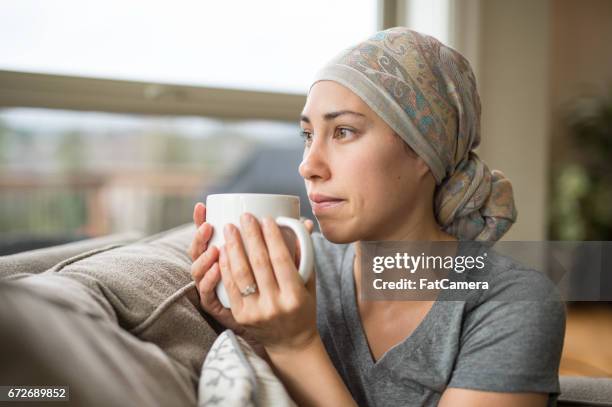 etnische jonge vrouw met kanker drinken kopje thee op de bank - headscarf home stockfoto's en -beelden