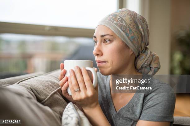 ethnic young woman with cancer drinking cup of tea on couch - cancer 2016 stock pictures, royalty-free photos & images