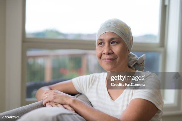volwassen etnische vrouw met kanker headwrap dragen op bank - headscarf home stockfoto's en -beelden