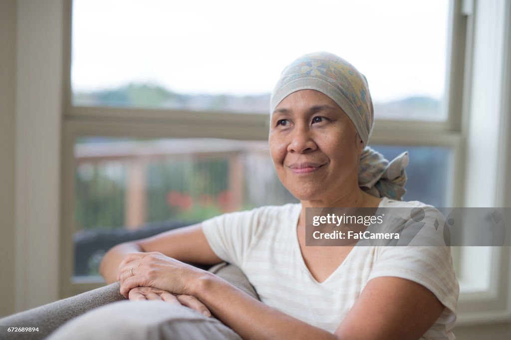 Mature ethnic woman with cancer wearing headwrap on couch