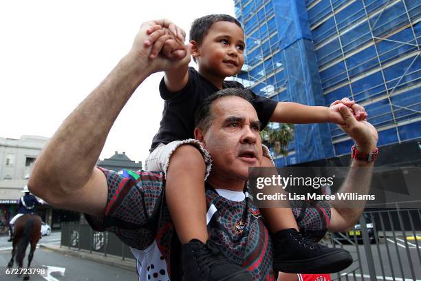 Indigenous man carries a young boy on his shoulders as he walks in the ANZAC march towards Redfern Park on April 25, 2017 in Sydney, Australia. The...