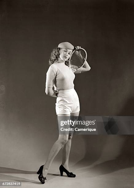 1940s 1950s YOUNG WOMAN WHITE SHORT SHORTS SWEATER BERET HOLDING TENNIS RACKET BEHIND HER BACK LOOKING AT CAMERA