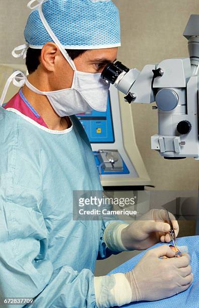 1990s MEDICAL OPERATION ROOM MAN DOCTOR PERFORMING EYE SURGERY USING BINOCULAR MICROSCOPE