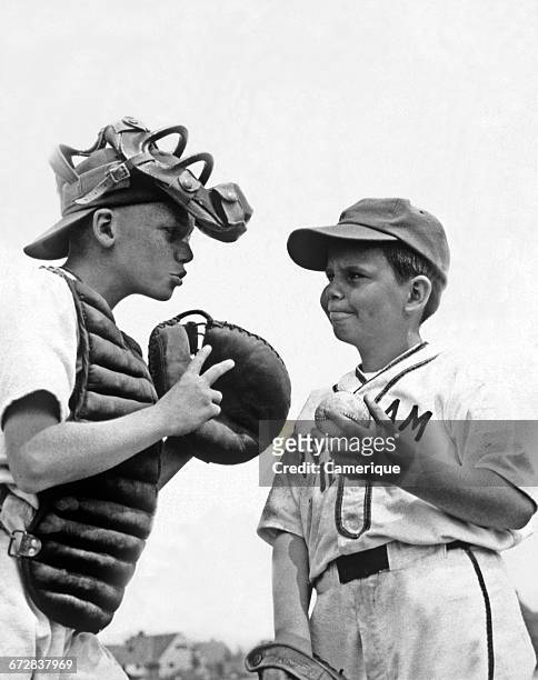 1950s TWO BOYS WEARING LITTLE LEAGUE BASEBALL UNIFORMS THE CATCHER IS GIVING ADVICE TO PITCHER