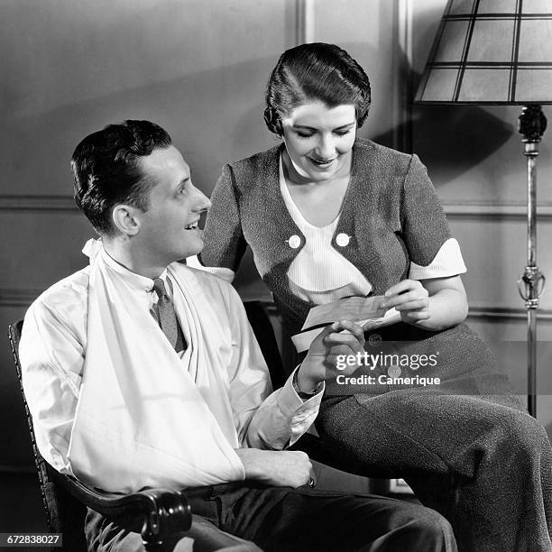 1930s COUPLE WOMAN HOLDING INSURANCE CHECK MAN WITH INJURED ARM IN SLING