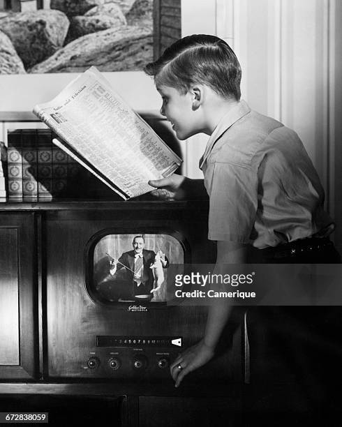 1940s BOY READING NEWSPAPER TV GUIDE ADJUSTING HIS TELEVISION TO CORRECT CHANNEL