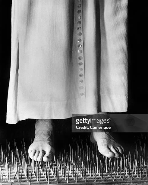 1950s 1960s MAN WALKING BAREFOOT ON BED OF NAILS
