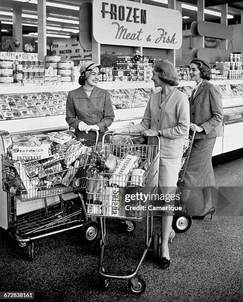 1950s THREE WOMEN PUSHING SHOPPING CARTS MEETING TALKING IN FROZEN FOOD AISLE OF SUPERMARKET