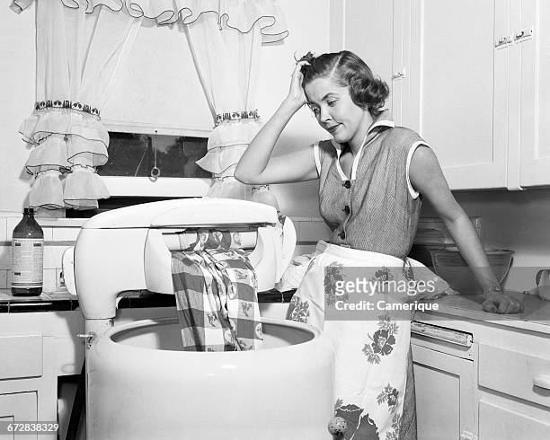 1950s FRUSTRATED HOUSEWIFE WITH JAMMED WRINGER ON CLOTHES WASHING MACHINE IN KITCHEN