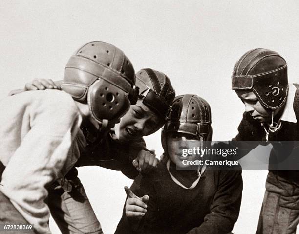 1930s GROUP OF BOYS WEARING LEATHER HELMETS IN HUDDLE PLAYING FOOTBALL