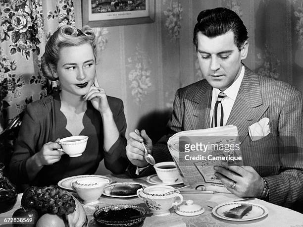 1940s COUPLE BREAKFAST TABLE IMPATIENT WOMAN LOOKING AT MAN READING NEWSPAPER