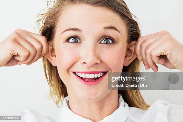 young woman pulling her ears, funny smile - portraits studio smile stockfoto's en -beelden