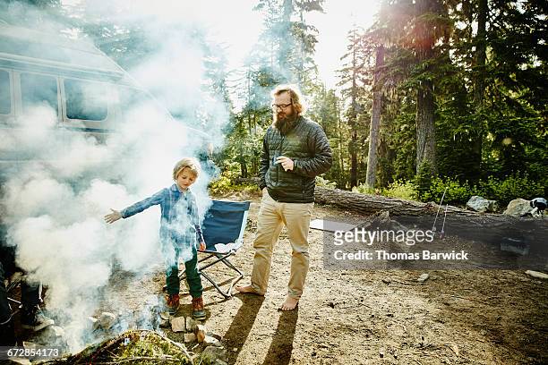 Young boy standing with father near campfire