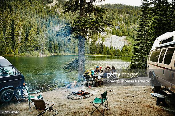 friends sharing a meal while camping by lake - tourisme vert photos et images de collection