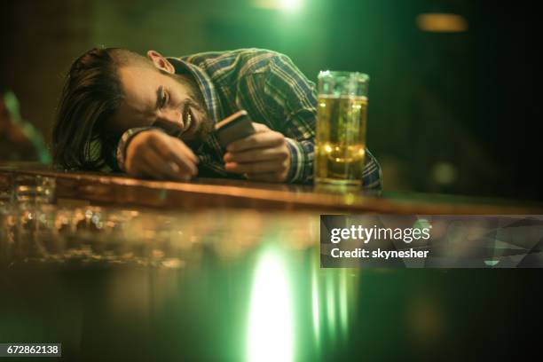 young wasted man text messaging on cell phone while leaning on a bar counter. - drunk guy stock pictures, royalty-free photos & images