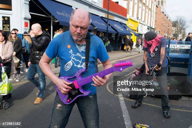 Two men on Portobello Road perform their busking performance to heavy rock music while pretending to play plastic toy guitars in London, England,...