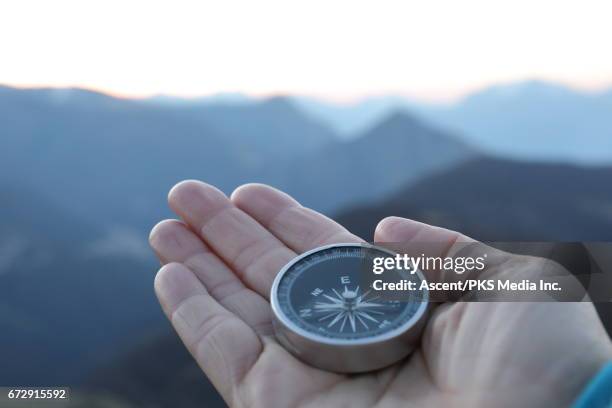 detail of hand holding compass on mountain summit - compass stock pictures, royalty-free photos & images