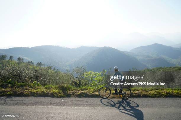 female bicyclist rides along road above hills, olive groves - country road side stock pictures, royalty-free photos & images