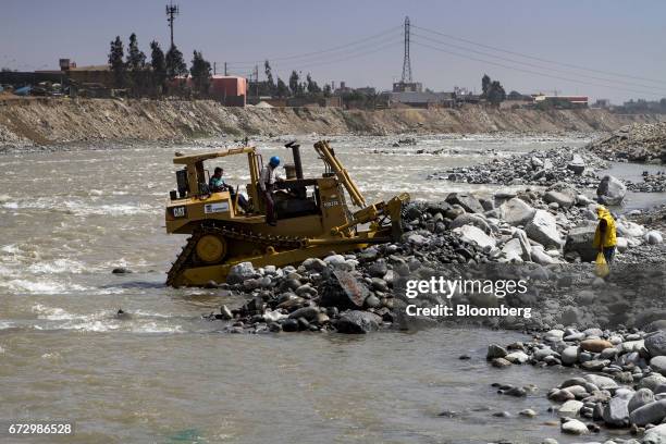 Workers operate a Caterpillar Inc. Machine to rebuild land impacted by massive floods in the town of Carapongo, Chosica district in Lima, Peru, on...